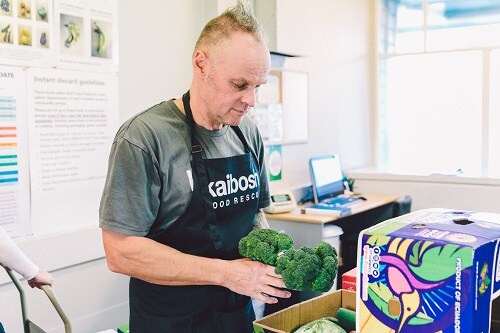 NZFN Food Hub, Kaibosh, staff member adding broccoli to a food parcel.