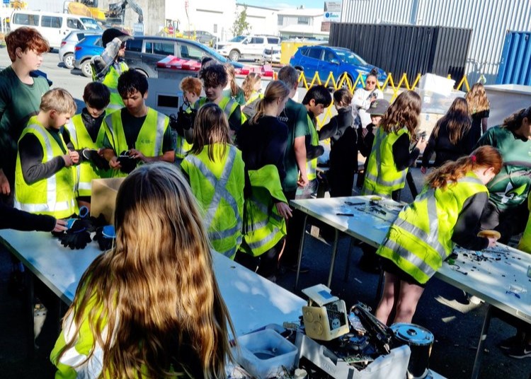 Group of kids learning electronics recycling outside on tables.