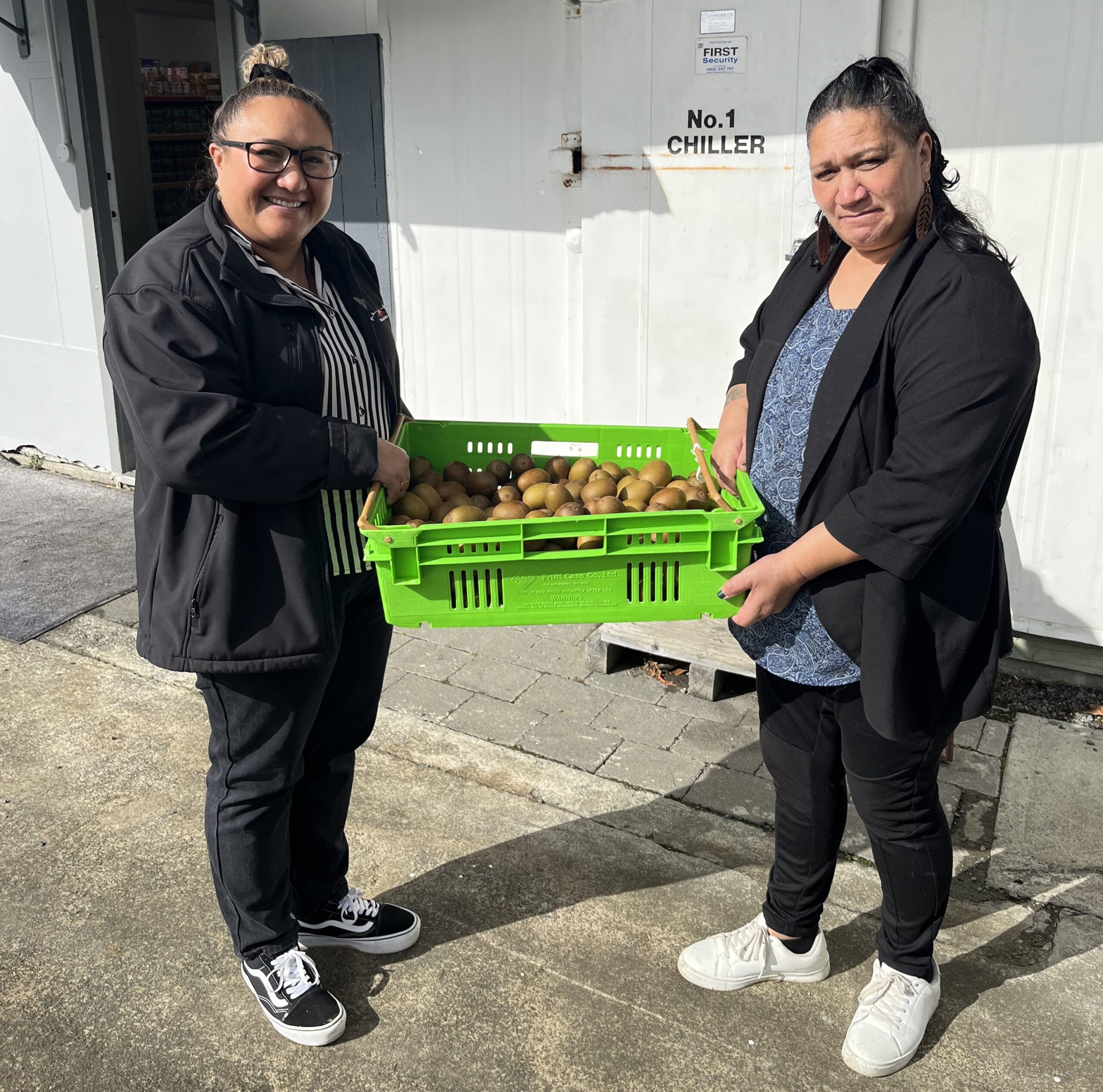 Te Hiku Pataka staff holding a donation of kiwifruit.